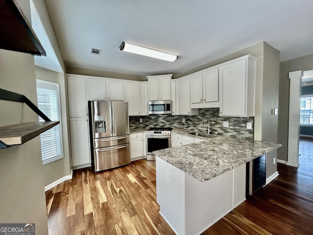 3988 Church View Ln, Suwanee, GA 30024 - kitchen with stainless steel appliances, wood finished floors, a peninsula, decorative backsplash, and white cabinets
