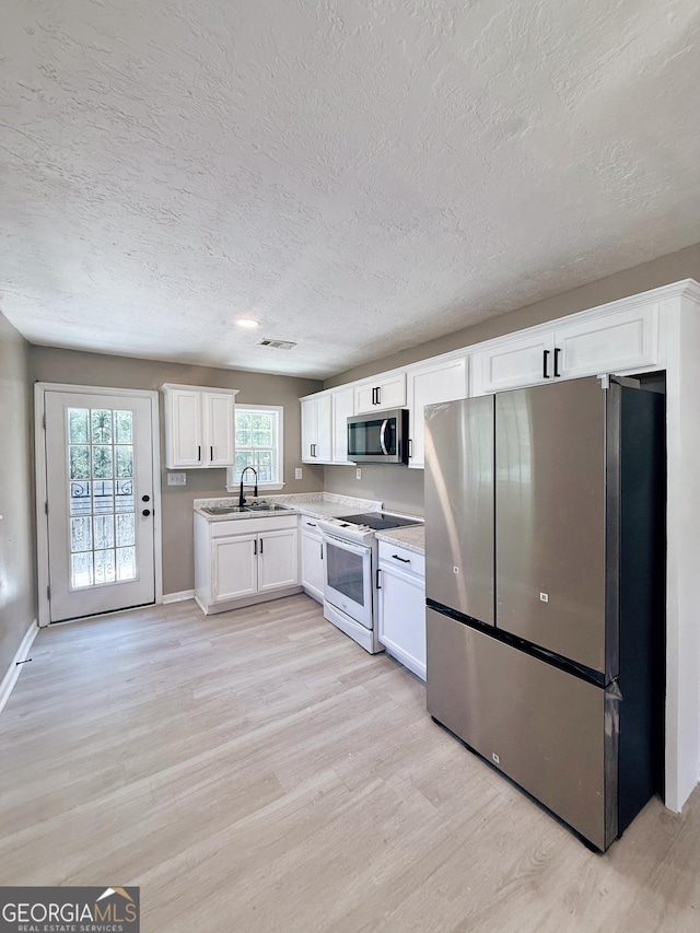 1502 12th St, Augusta, GA 30901 - kitchen featuring stainless steel appliances, light wood-style floors, a textured ceiling, a sink, and white cabinetry