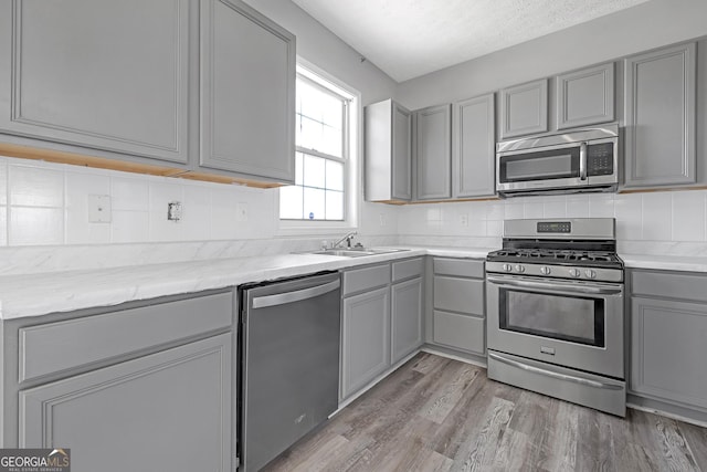 145 Silver Mine Trl, Austell, GA 30168 - kitchen with appliances with stainless steel finishes, gray cabinets, a sink, light wood-style floors, and backsplash