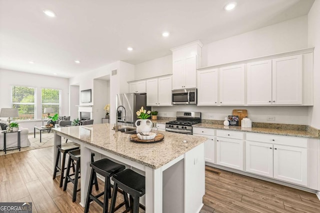 1172 Edwin Ln, Sugar Hill, GA 30518 - kitchen featuring stainless steel appliances, white cabinetry, a center island with sink, a kitchen breakfast bar, and wood finished floors