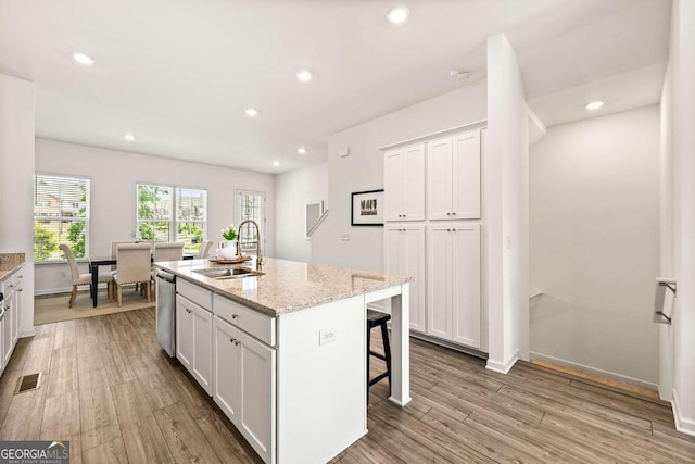 1172 Edwin Ln, Sugar Hill, GA 30518 - kitchen with white cabinetry, light wood-style flooring, a breakfast bar, light stone countertops, and a center island with sink