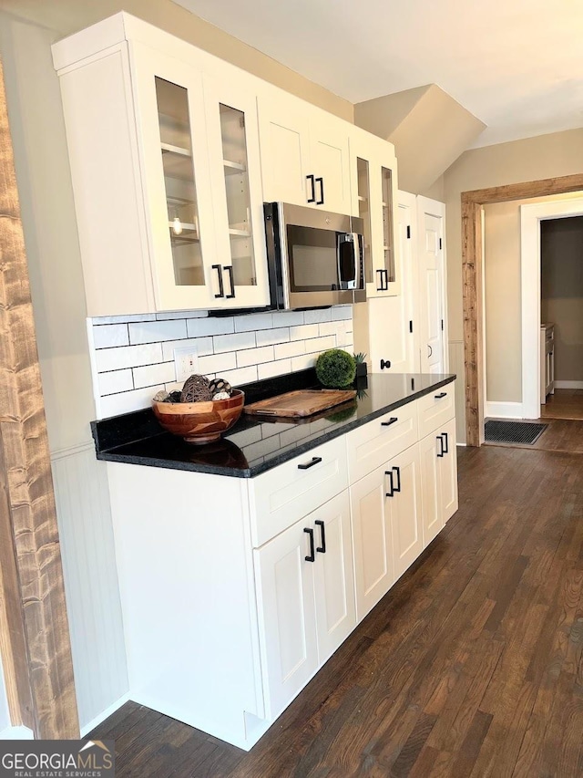 125 Oak Ave, Carrollton, GA 30117 - kitchen featuring stainless steel microwave, dark countertops, decorative backsplash, dark wood-type flooring, and glass insert cabinets