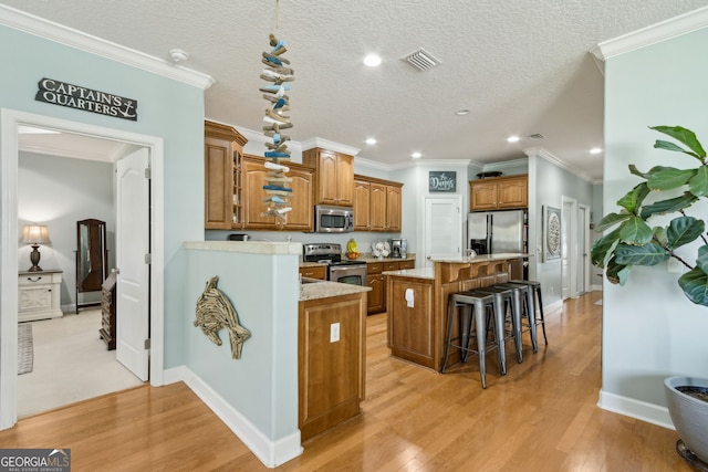 247 Laurel Landing Blvd, Kingsland, GA 31548 - kitchen with stainless steel appliances, a center island, brown cabinetry, a breakfast bar, and light wood-style flooring