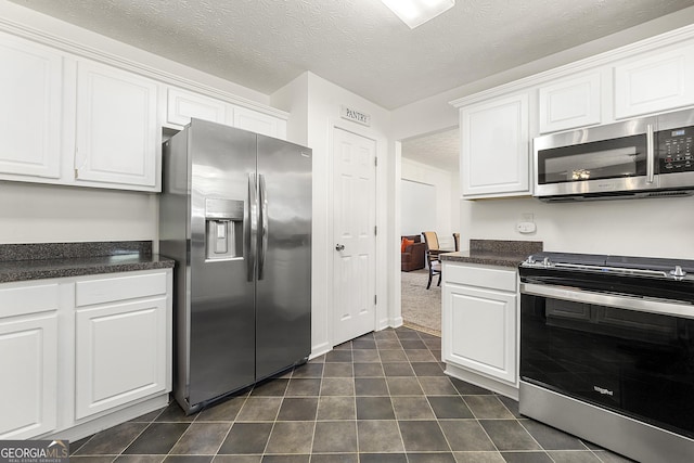 5125 Winding Glen Dr, Lithonia, GA 30038 - kitchen featuring stainless steel appliances, dark countertops, white cabinets, dark tile patterned flooring, and a textured ceiling