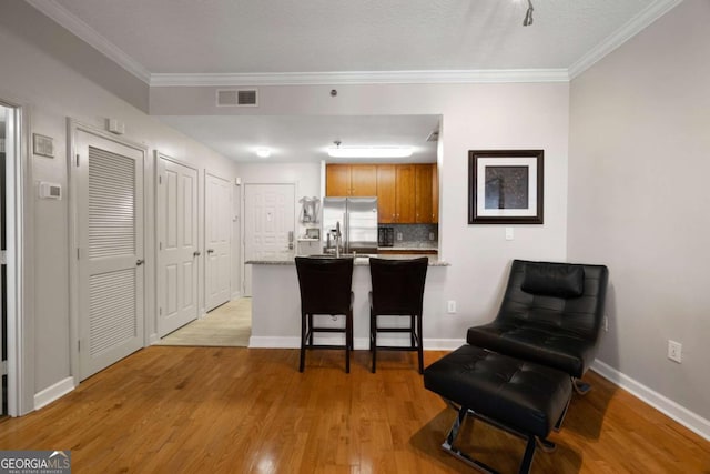 1101 Juniper St NE Unit 1216, Atlanta, GA 30309 - kitchen with stainless steel fridge, a peninsula, light wood-type flooring, tasteful backsplash, and ornamental molding