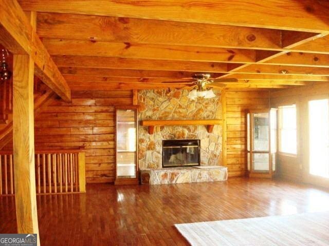 697 Waddell Rd, Woodbury, GA 30293 - unfurnished living room featuring beamed ceiling, wood walls, ceiling fan, a stone fireplace, and wood finished floors