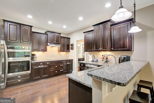 108 Hidden Springs Dr, Lagrange, GA 30240 - kitchen featuring stainless steel appliances, under cabinet range hood, a breakfast bar area, light stone counters, and backsplash