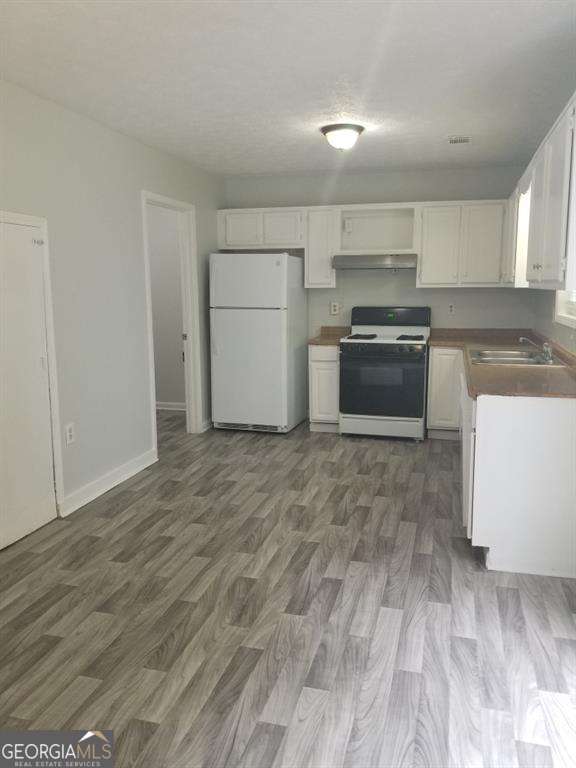 3530 Hopkins Ct, Powder Springs, GA 30127 - kitchen featuring gas range, freestanding refrigerator, under cabinet range hood, white cabinetry, and dark wood-type flooring