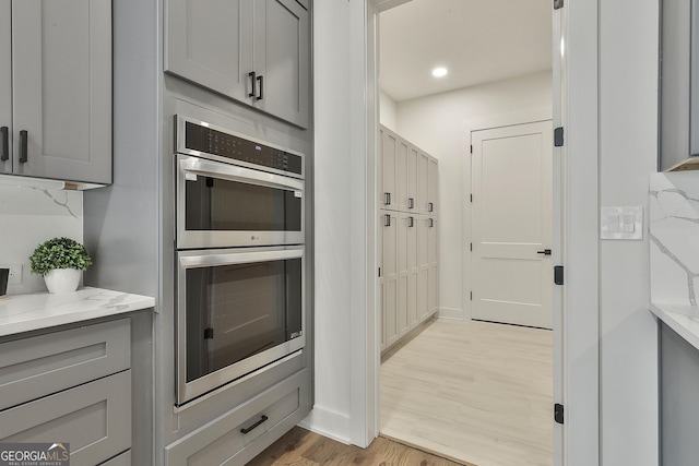1240 Hayes Sq, Peachtree City, GA 30269 - kitchen featuring stainless steel double oven, gray cabinetry, light wood-style floors, light stone countertops, and baseboards