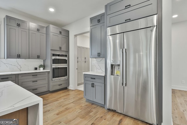 1240 Hayes Sq, Peachtree City, GA 30269 - kitchen featuring appliances with stainless steel finishes, gray cabinets, light stone counters, light wood-type flooring, and recessed lighting