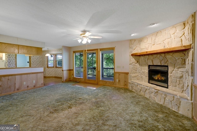 156 Spoon Hill Dr, Hayesville, NC 28904 - unfurnished living room featuring a ceiling fan, carpet floors, a stone fireplace, a wainscoted wall, and wooden walls