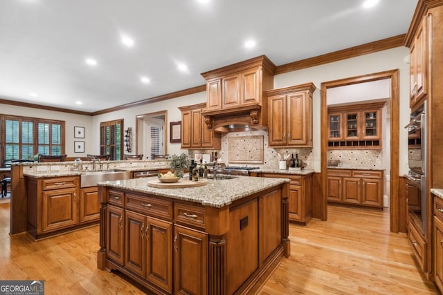 13037 Overlook Pass, Roswell, GA 30075 - kitchen featuring an island with sink, a sink, brown cabinetry, ornamental molding, and light wood-style floors