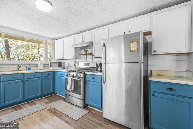 2826 Ben Hill Rd, East Point, GA 30344 - kitchen with stainless steel appliances, blue cabinetry, under cabinet range hood, a textured ceiling, and light wood finished floors