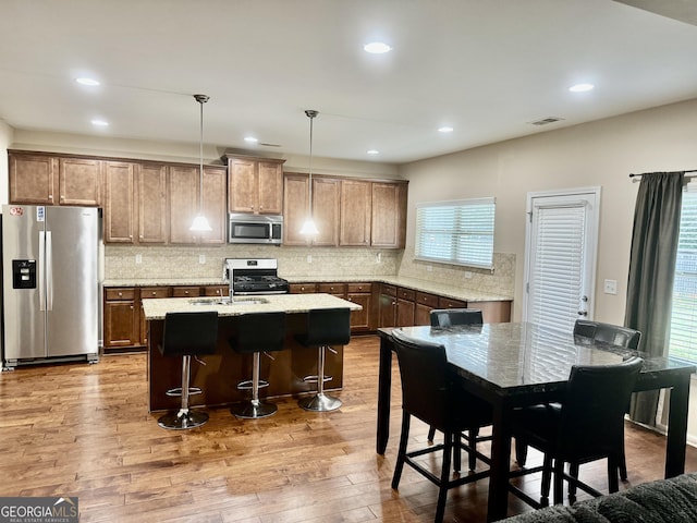 9108 Alden Dr, Locust Grove, GA 30248 - kitchen with stainless steel appliances, an island with sink, light wood-type flooring, backsplash, and a kitchen breakfast bar