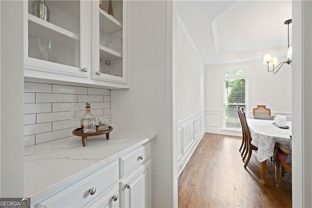 4108 Wyndam Hill Dr, Suwanee, GA 30024 - bar area with decorative backsplash, a raised ceiling, a chandelier, wainscoting, and wood finished floors