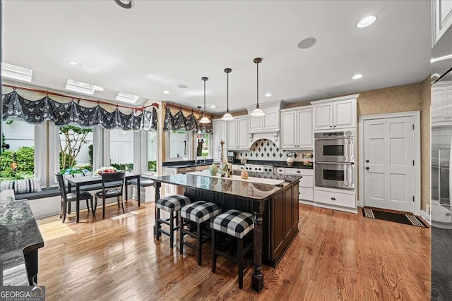 162 Daltree Ct, Marietta, GA 30068 - kitchen with dark countertops, stainless steel double oven, light wood-style floors, white cabinetry, and an island with sink