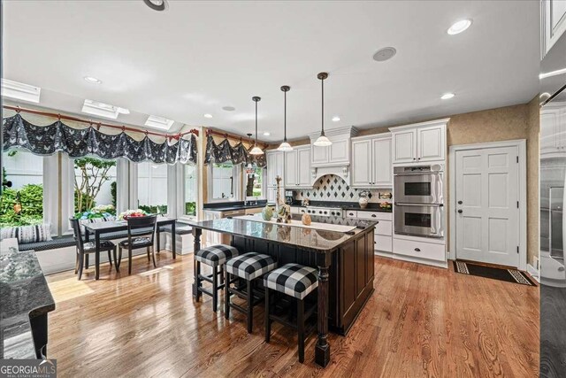 162 Daltree Ct, Marietta, GA 30068 - kitchen featuring dark countertops, double oven, light wood-style floors, white cabinetry, and a kitchen island