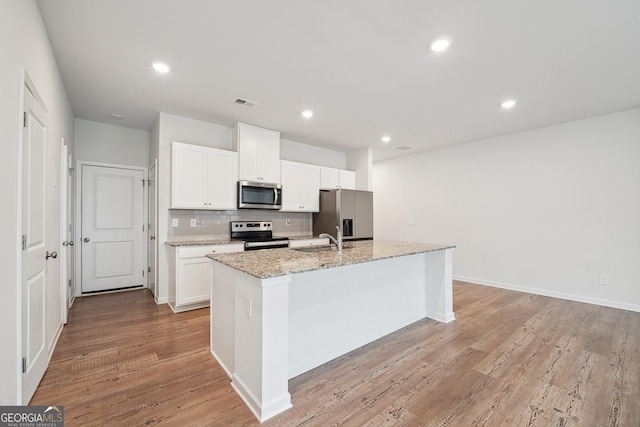 5207 Canberra Dr, Flowery Branch, GA 30542 - kitchen with stainless steel appliances, a center island with sink, tasteful backsplash, white cabinets, and light wood-style floors
