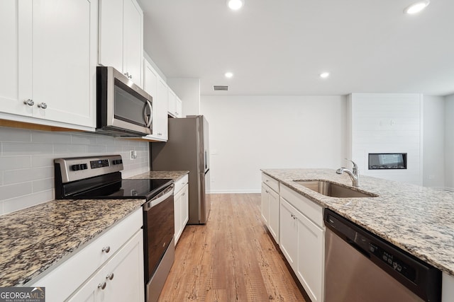5207 Canberra Dr, Flowery Branch, GA 30542 - kitchen with appliances with stainless steel finishes, light wood-style flooring, white cabinets, decorative backsplash, and light stone counters
