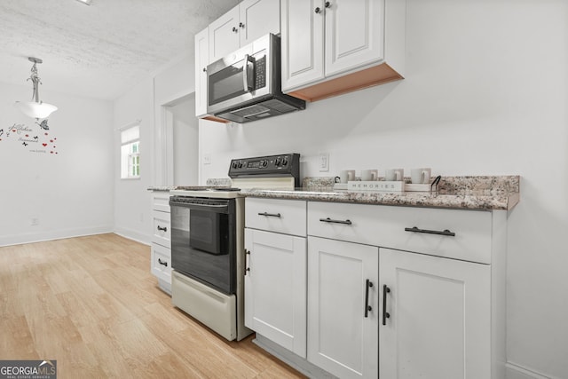 6802 Ida St, Lithonia, GA 30058 - kitchen with black electric range oven, stainless steel microwave, a textured ceiling, white cabinets, and light wood-style flooring