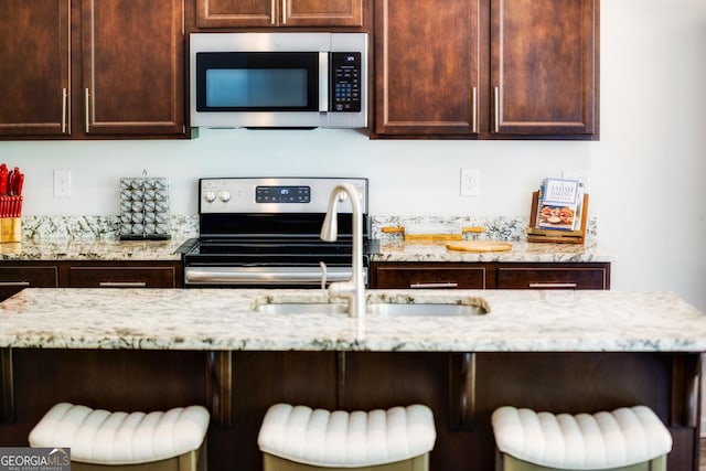 104 Johansen Way, Kingsland, GA 31548 - kitchen with stainless steel appliances, a kitchen bar, dark brown cabinets, and light stone counters