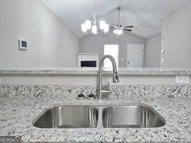 3075 Lakeside Cir, Covington, GA 30016 - kitchen view of a sink, a chandelier, a fireplace, light stone counters, and a ceiling fan
