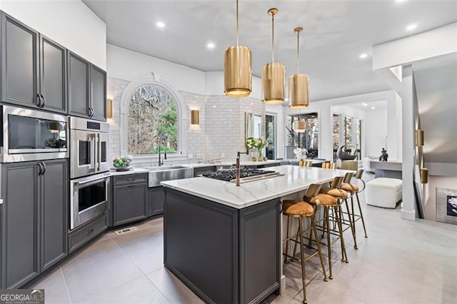 8610 Sentinae Chase Dr, Roswell, GA 30076 - kitchen with appliances with stainless steel finishes, a breakfast bar area, gray cabinets, light stone countertops, and a kitchen island with sink