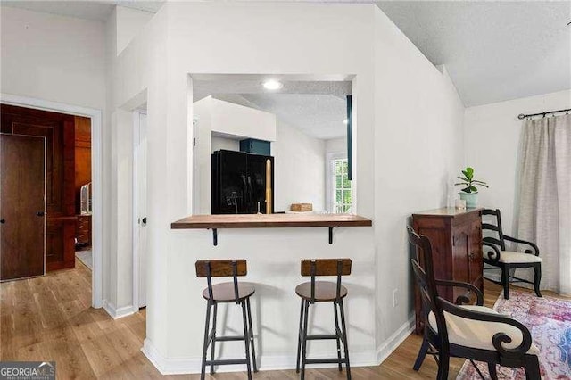374 Dooley Rd, Dallas, GA 30132 - kitchen with black fridge with ice dispenser, wood finished floors, a kitchen bar, baseboards, and lofted ceiling