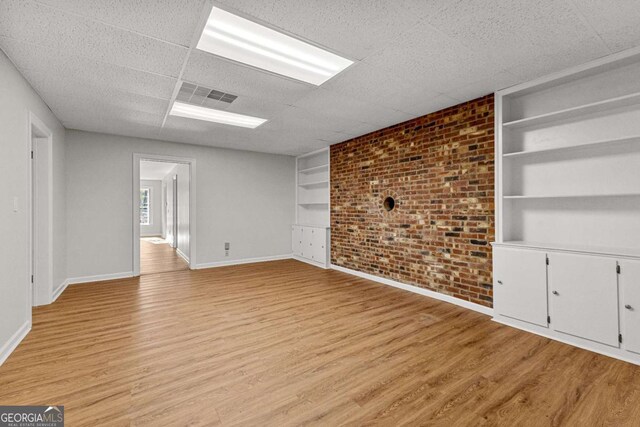 135 Mill Race Rd, Thomaston, GA 30286 - unfurnished living room featuring built in features, baseboards, light wood-style flooring, brick wall, and a drop ceiling