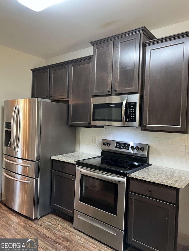 1010 Holliday Pass, Griffin, GA 30223 - kitchen featuring stainless steel appliances, wood finished floors, tasteful backsplash, light stone countertops, and dark brown cabinets