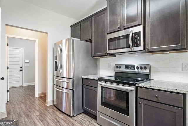 1010 Holliday Pass, Griffin, GA 30223 - kitchen featuring stainless steel appliances, decorative backsplash, light stone counters, light wood-style flooring, and dark brown cabinets