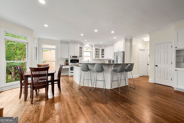 3714 Westbrooke Cir, Brookhaven, GA 30319 - kitchen featuring stainless steel appliances, white cabinetry, a kitchen breakfast bar, glass insert cabinets, and ornamental molding
