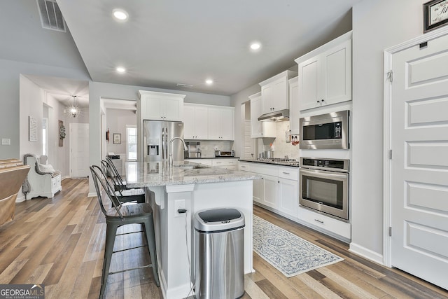 390 Cushing St, Senoia, GA 30276 - kitchen with stainless steel appliances, a sink, wood finished floors, white cabinets, and a breakfast bar