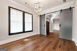 320 Dodd Ln, Alpharetta, GA 30005 - unfurnished dining area featuring a barn door, baseboards, wood finished floors, and crown molding