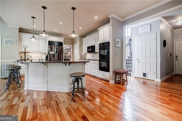 3620 Chartwell Dr, Suwanee, GA 30024 - kitchen featuring black appliances, a breakfast bar, dark countertops, light wood finished floors, and white cabinetry