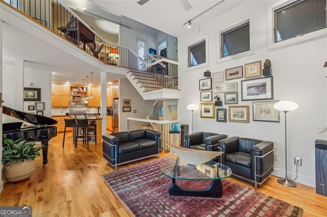6550 Bluewaters Dr, Flowery Branch, GA 30542 - living room featuring a high ceiling, light wood-style flooring, stairs, track lighting, and a ceiling fan