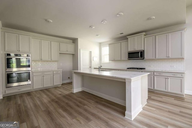 2856 Knob Creek Dr, Snellville, GA 30078 - kitchen with appliances with stainless steel finishes, a sink, decorative backsplash, light wood-style floors, and a center island with sink