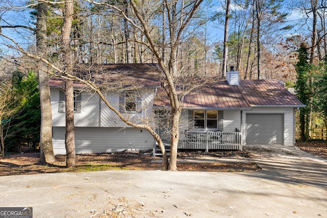 7000 Woodland Pl NW, Kennesaw, GA 30152 - split level home featuring an attached garage, concrete driveway, a chimney, a metal roof, and covered porch