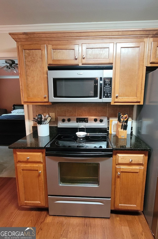 135 Pine Creek Way, Winterville, GA 30683 - kitchen with appliances with stainless steel finishes, light wood finished floors, dark stone counters, ceiling fan, and crown molding