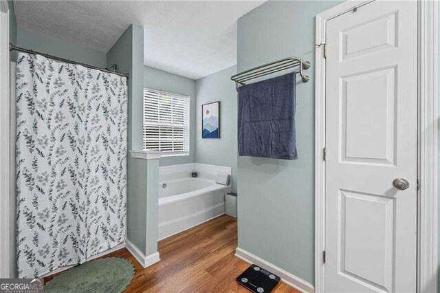 1047 Woodsong Pass Ct, Lawrenceville, GA 30043 - full bath featuring wood finished floors, a garden tub, a shower with curtain, baseboards, and a textured ceiling