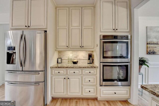 3760 Ansley Park Dr, Suwanee, GA 30024 - kitchen with appliances with stainless steel finishes, cream cabinets, decorative backsplash, light stone counters, and crown molding
