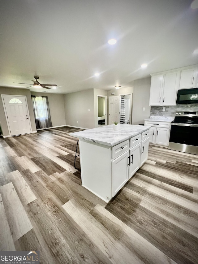 1962 Anderson Rd, Rentz, GA 31075 - kitchen with stainless steel electric stove, black microwave, light wood finished floors, a center island, and white cabinets