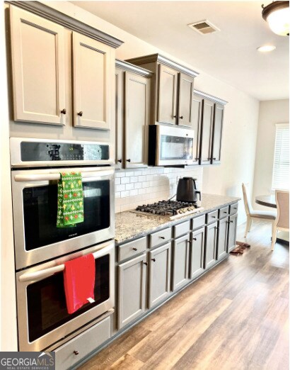 413 Atlas Ct, Locust Grove, GA 30248 - kitchen featuring stainless steel appliances, decorative backsplash, light wood-style floors, light stone countertops, and gray cabinets