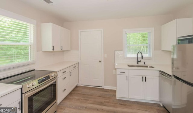 525 Baker Cir NW, Atlanta, GA 30318 - kitchen featuring appliances with stainless steel finishes, a sink, light wood-type flooring, white cabinetry, and tasteful backsplash
