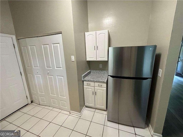 5422 Timor Trl, Lithonia, GA 30038 - kitchen featuring freestanding refrigerator, light tile patterned floors, white cabinetry, baseboards, and light stone counters