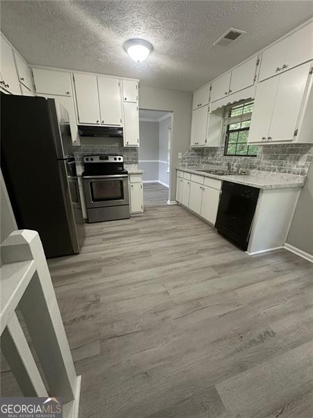 5388 Robertson Path, Lithonia, GA 30038 - kitchen with appliances with stainless steel finishes, light wood-style floors, white cabinetry, and a textured ceiling