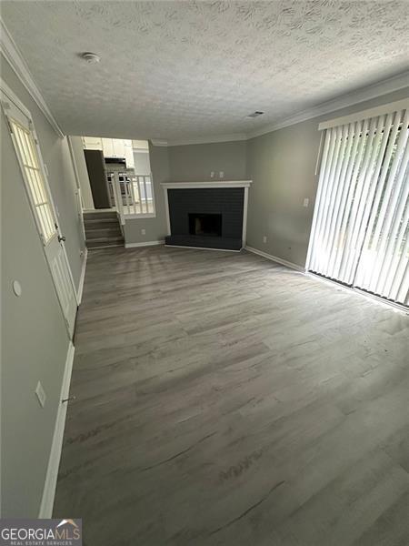 5388 Robertson Path, Lithonia, GA 30038 - unfurnished living room featuring baseboards, crown molding, a textured ceiling, wood finished floors, and a fireplace with raised hearth