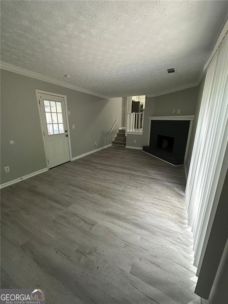 5388 Robertson Path, Lithonia, GA 30038 - unfurnished living room featuring a textured ceiling, baseboards, stairs, ornamental molding, and a fireplace with raised hearth
