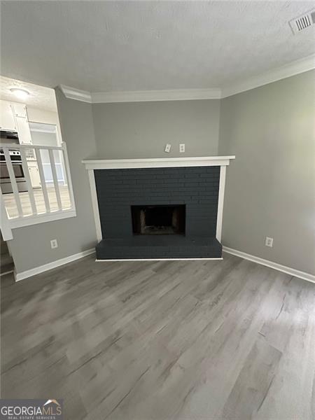 5388 Robertson Path, Lithonia, GA 30038 - unfurnished living room with baseboards, crown molding, a brick fireplace, and wood finished floors