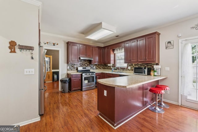 1093 Forest View Ln SW, Lilburn, GA 30047 - kitchen featuring appliances with stainless steel finishes, under cabinet range hood, a peninsula, backsplash, and light countertops